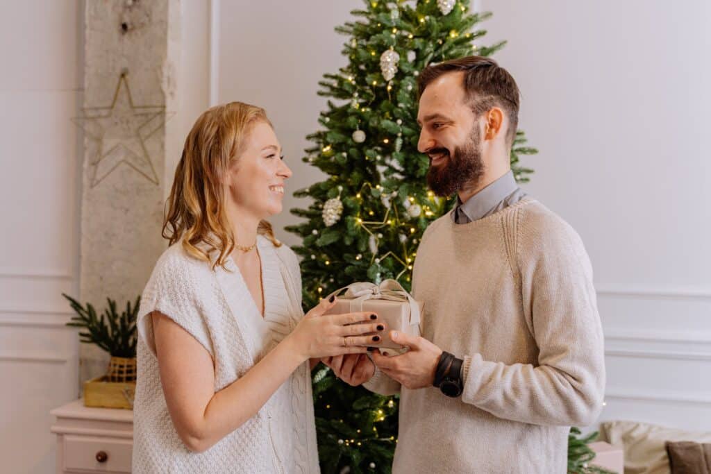 a-man-giving-a-present-to-a-woman-standing-in-front-of-a-christmas-tree-smiling