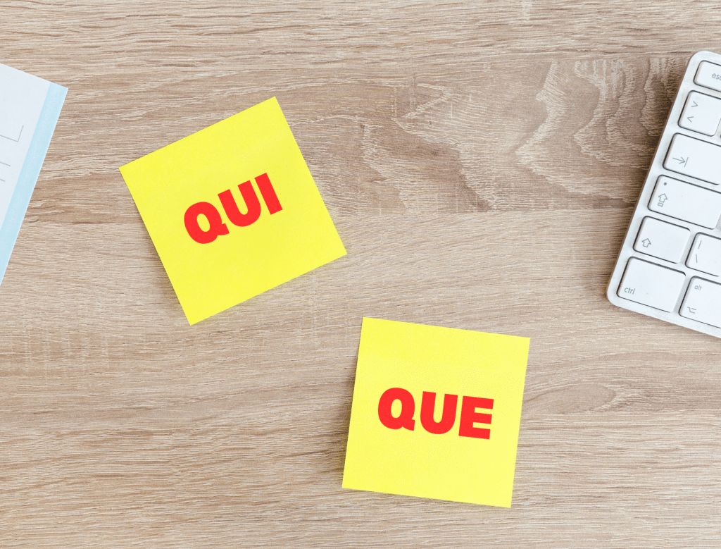 two-yellow-sticky-notes-with-the-french-words-qui-and-que-on-them-against-wooden-grain-table-background