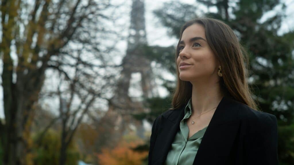 A young woman stands in front of the Eiffel Tower