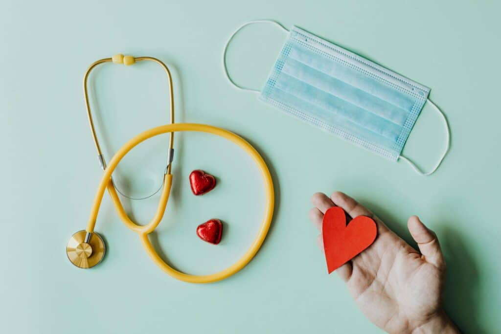 photo-of-stethoscope-face-mask-and-hand-holding-red-paper-heart