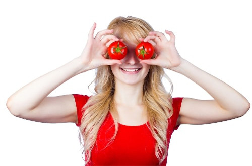A smiling woman holding tomatoes in front of her eyes