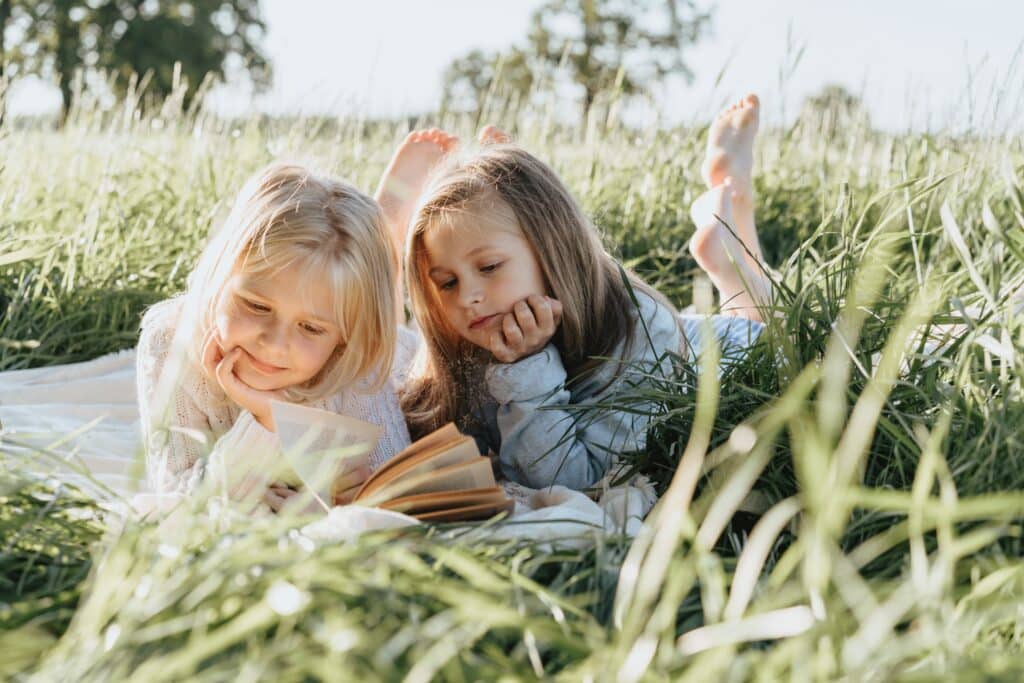 two-little-girls-reading-book-in-field