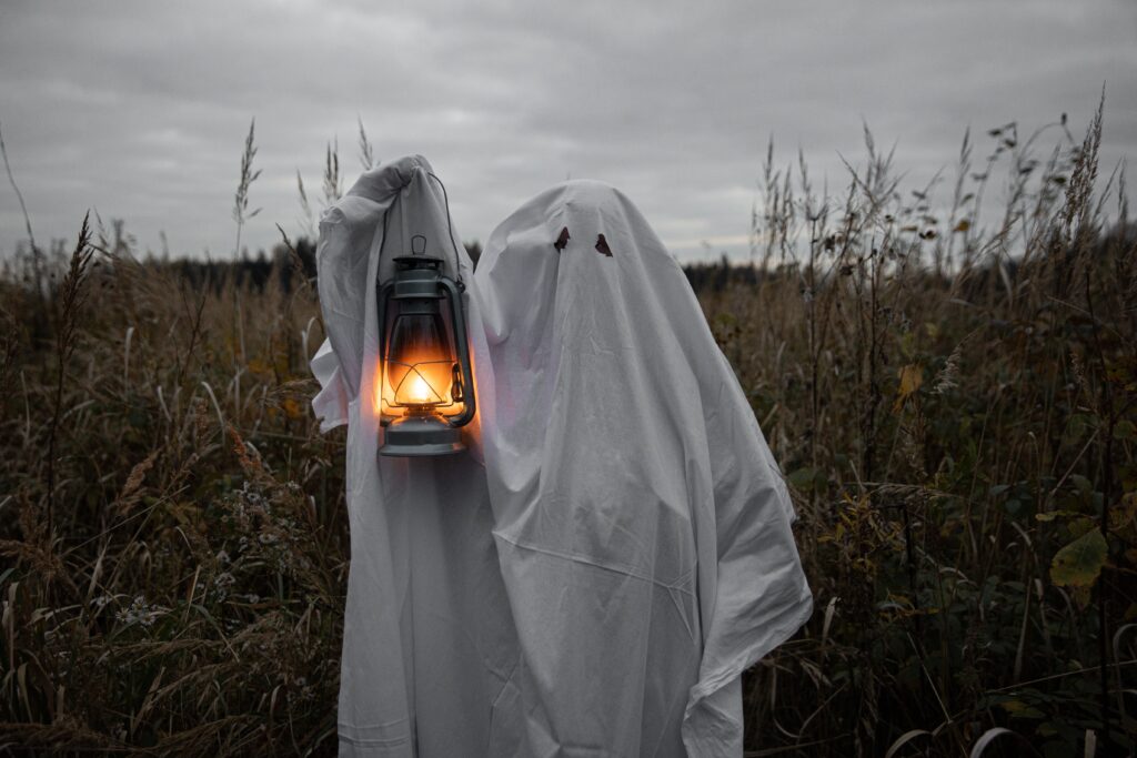 A person dressed as a ghost, holding a lantern