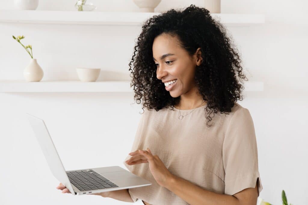woman-with-afro-hairstyle-smiling-while-holding-laptop-in-arm