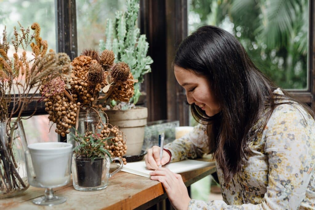picture-of-a-woman-smiling-while-writing-in-a-notebook-surrounded-by-plants
