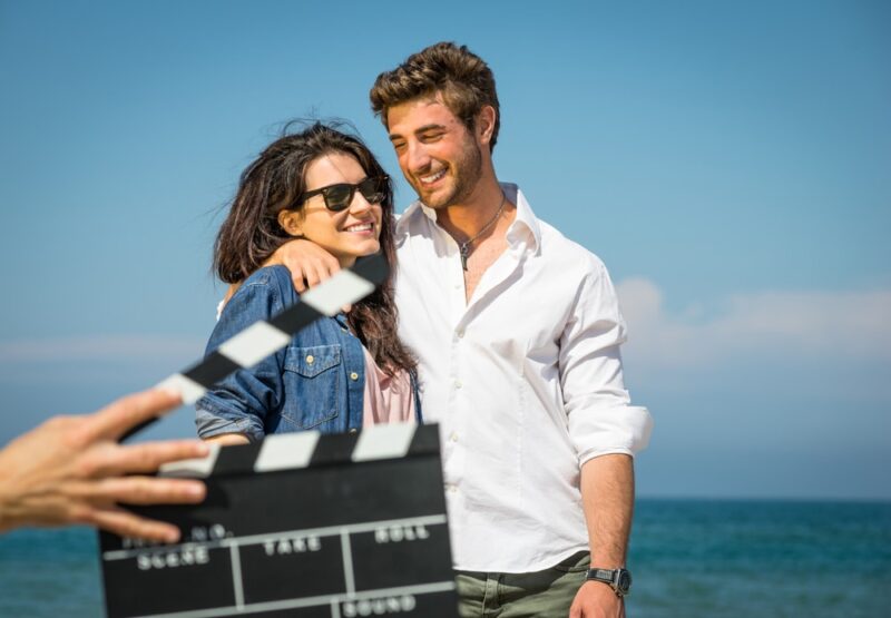 man and woman actor hugging in front of the ocean on the set of a movie scene