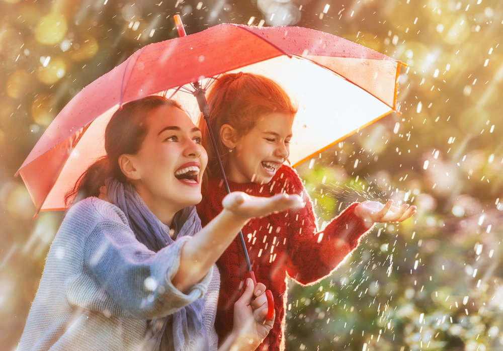 A happy woman and girl under an umbrella, catching raindrops on their hands.