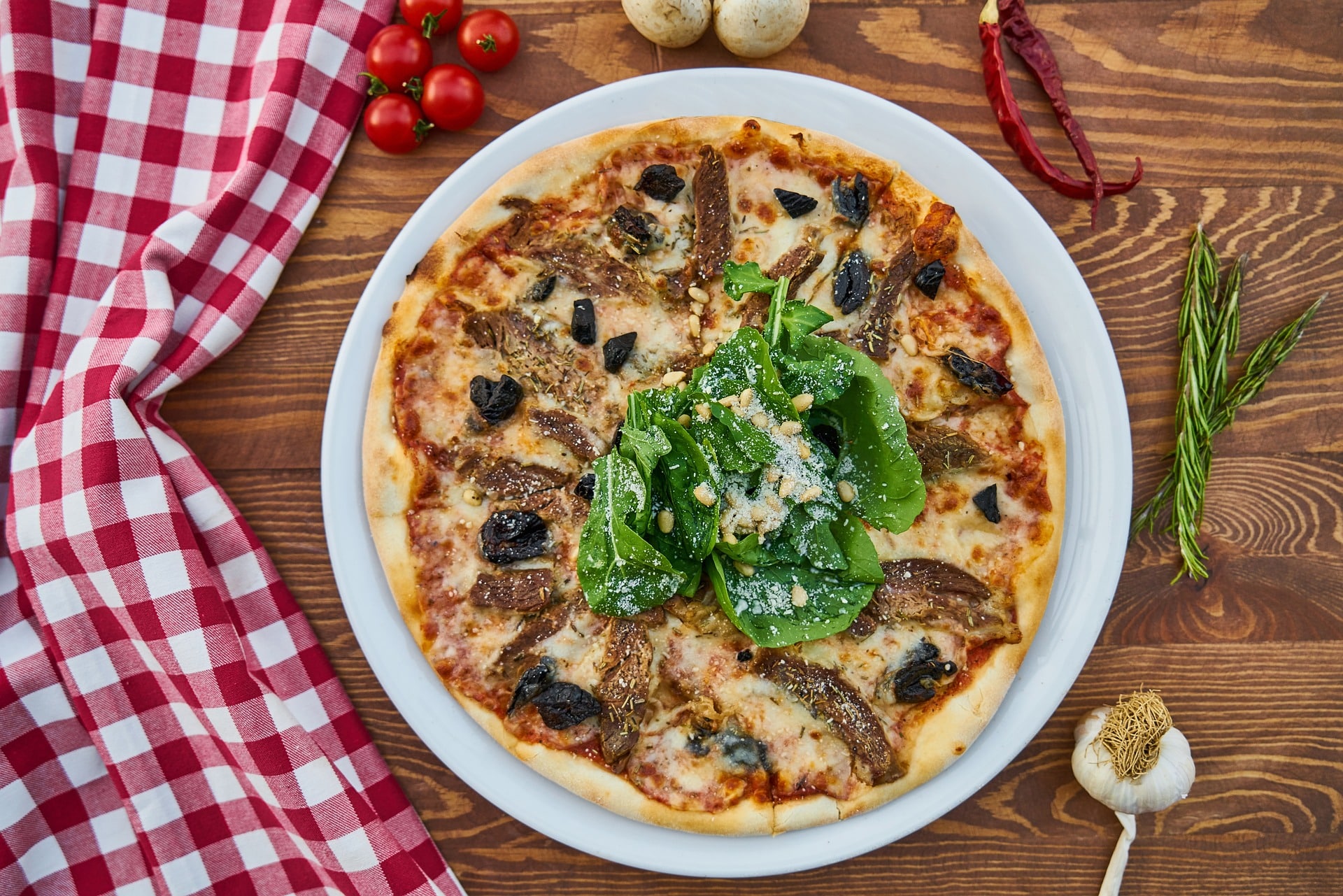 pizza-on-a-plate-on-a-wooden-table-surrounded-by tomatoes-mushrooms-herbs-and-garlic