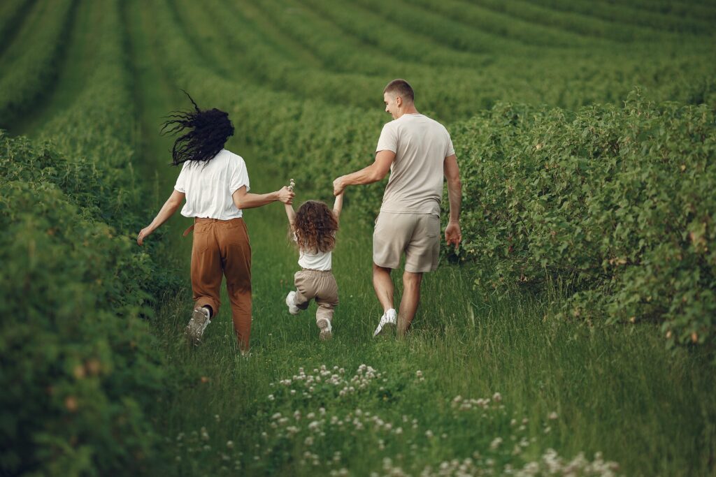 happy-parents-with-child-running-through-a-green-field-pexels