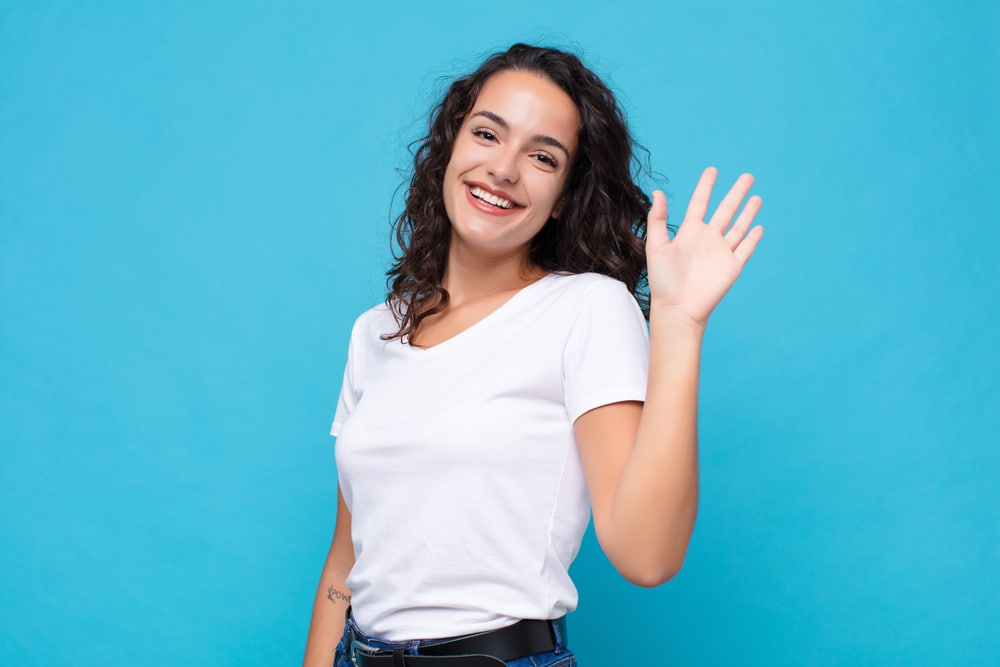young woman waving goodbye standing against a blue background
