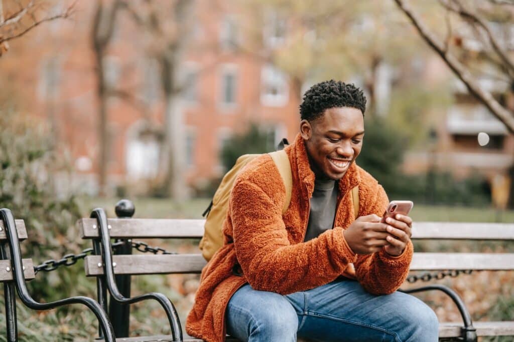 smiling-man-of-african-descent-sitting-on-bench-playing-games-on-mobile-phone