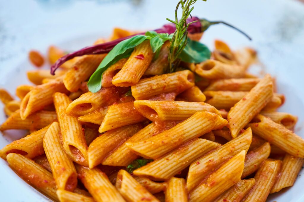 close-up-photo-of-cooked-penne-pasta-in-red-sauce-garnished-with-leaves-and-chili