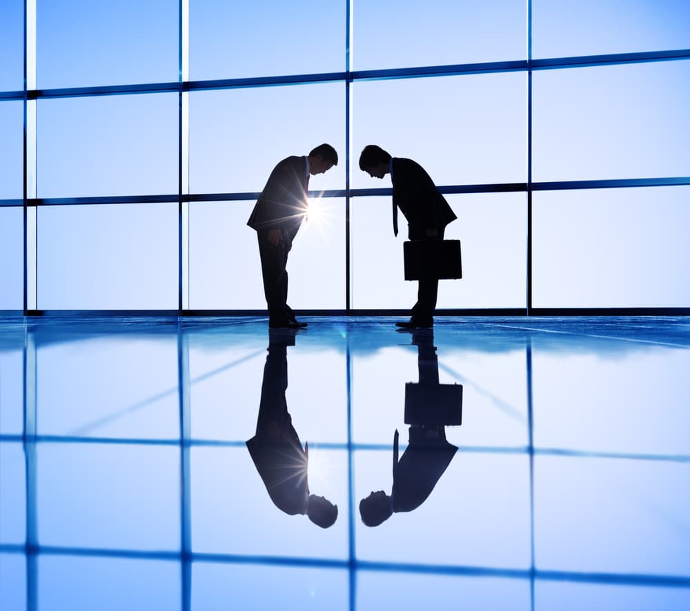 A decorative image of two men bowing to each other in front of a huge glass window.