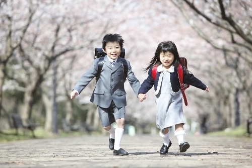 A young Japanese boy and girl wearing school uniforms and randsel backpacks