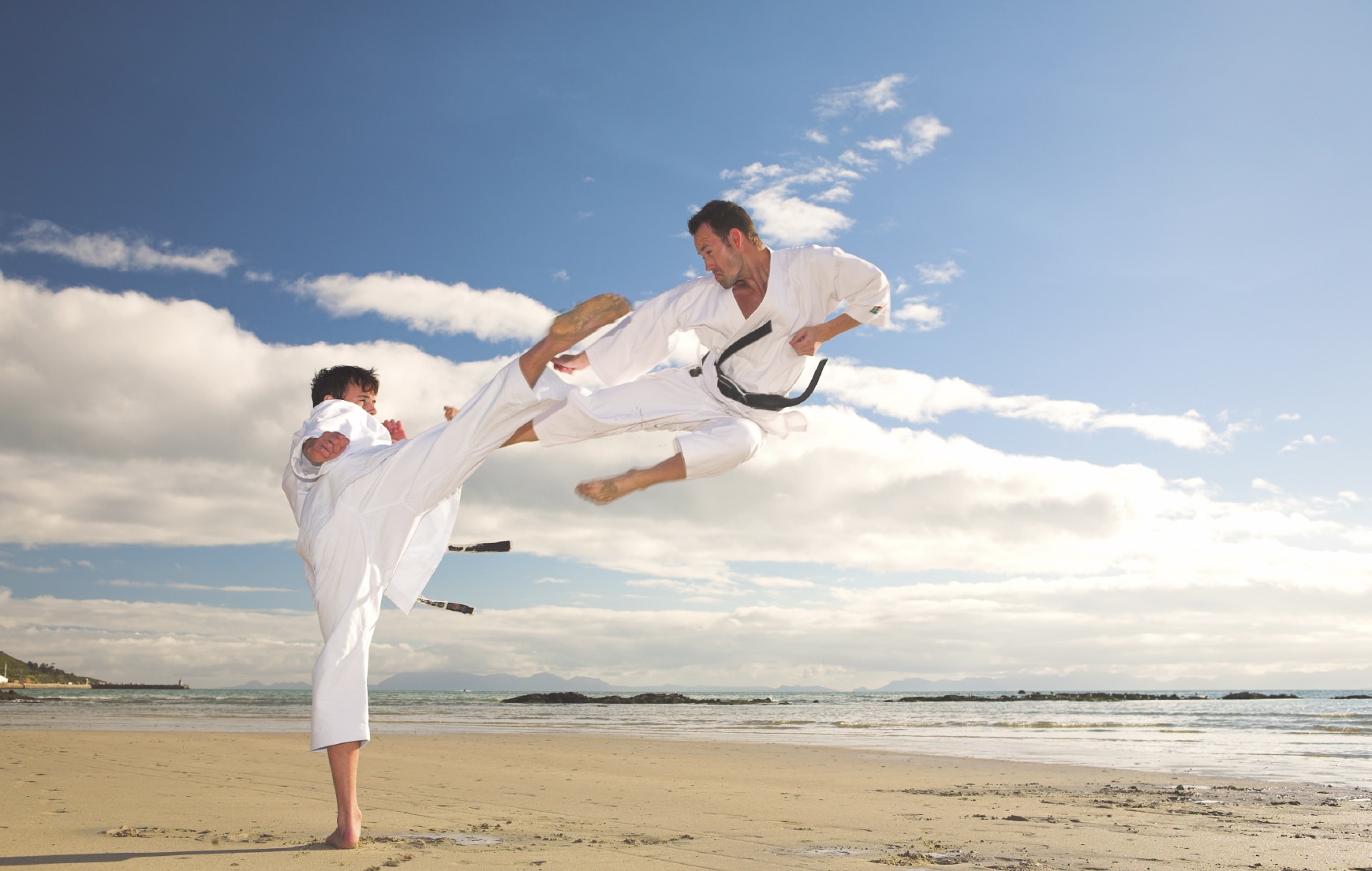 Two men in white gi doing karate on a beach
