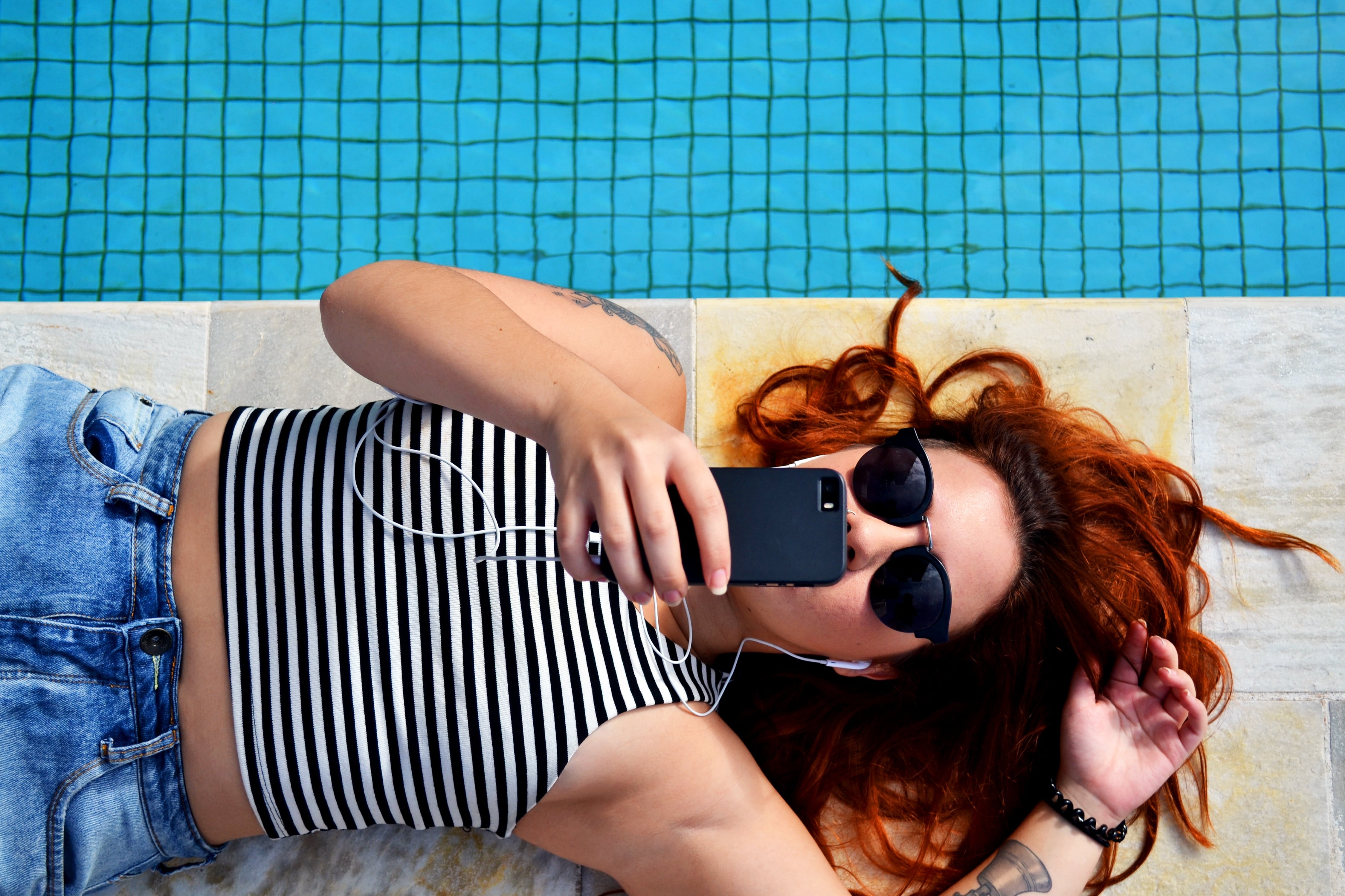 Woman lying down looking at phone wearing sunglasses