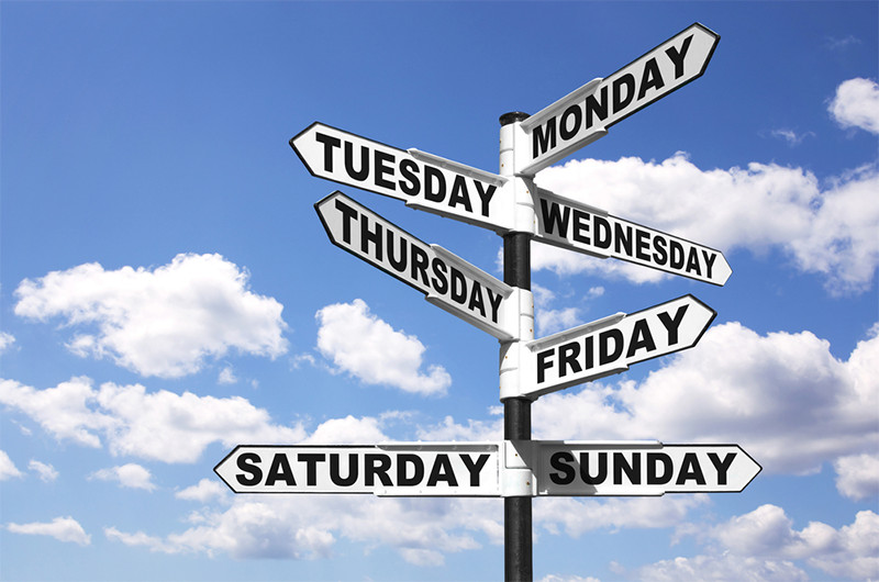road sign pointing different directions with names of the days of the week