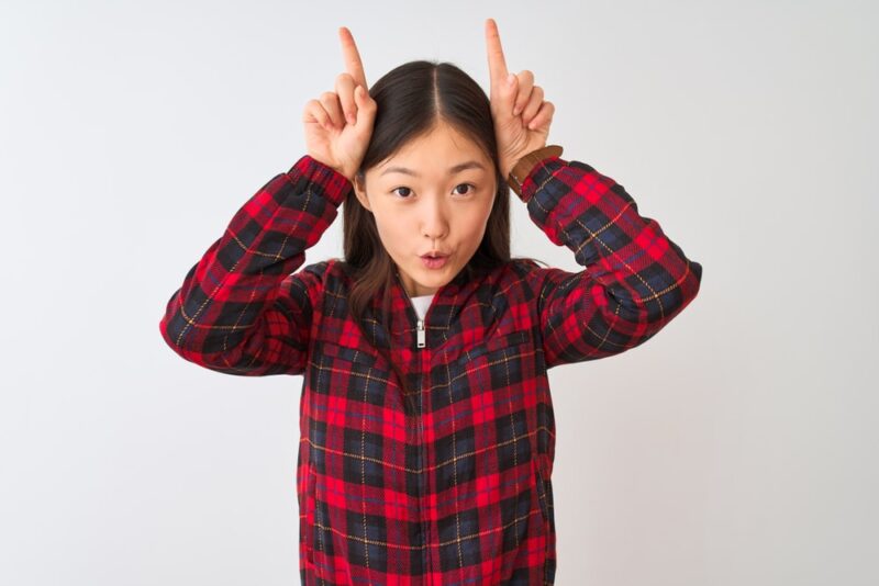 asian-woman-doing-funny-gesture-with-finger-over-head-as-bull-horns