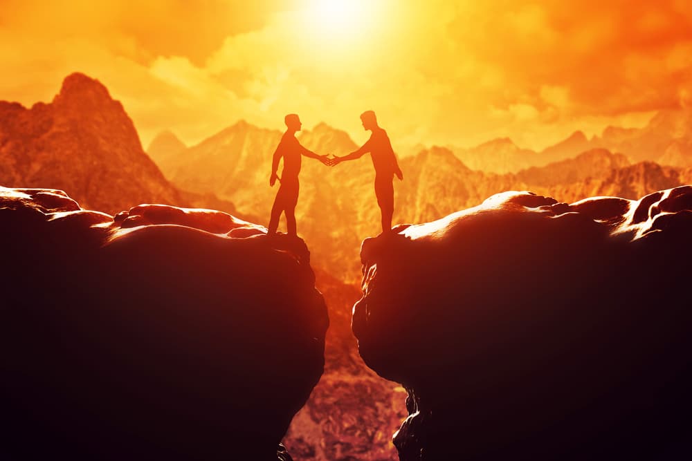 two man shaking hands at sunset on a rocky outcrop