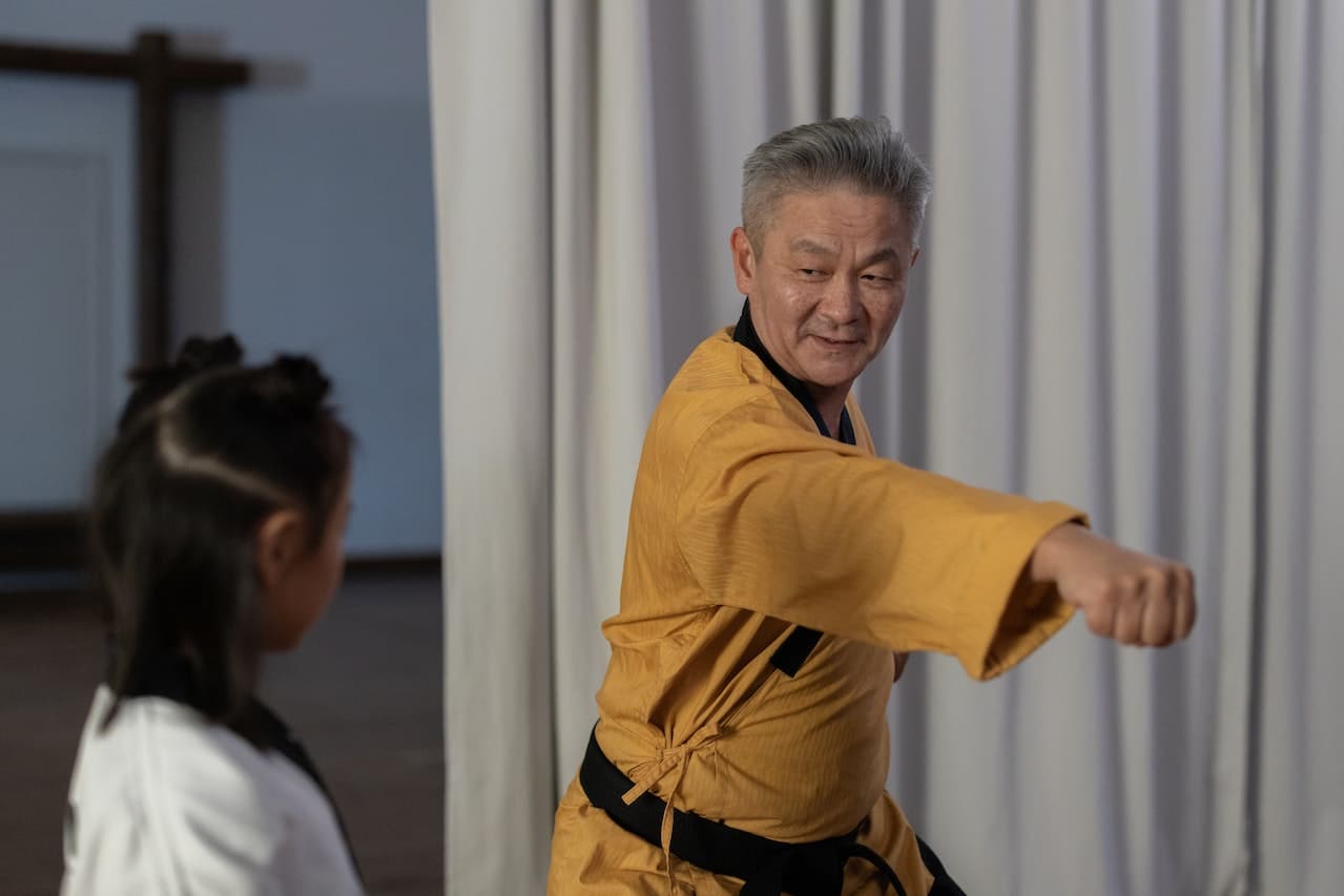 Man in yellow gi demonstrates martial arts move to young female student