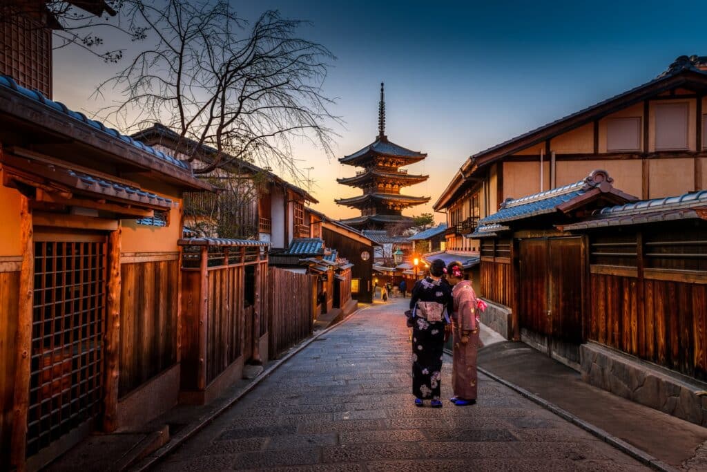 Two women in Japanese traditional dress stroll down a street toward a temple in Kyoto