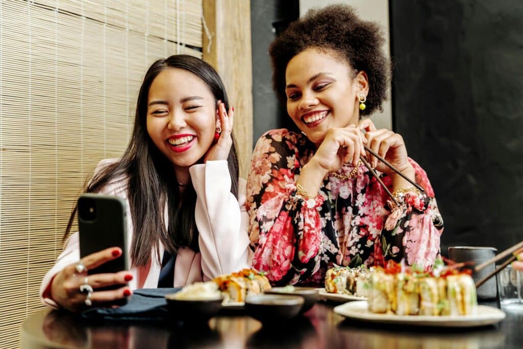 asian-and-black-woman-taking-selfie-and-smiling-while-eating-in-japanese-restaurant