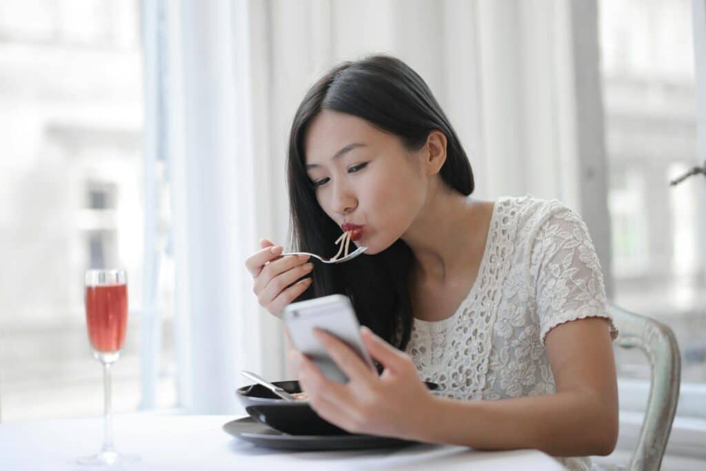 asian-woman-eating-noodles-as-she-looks-at-phone