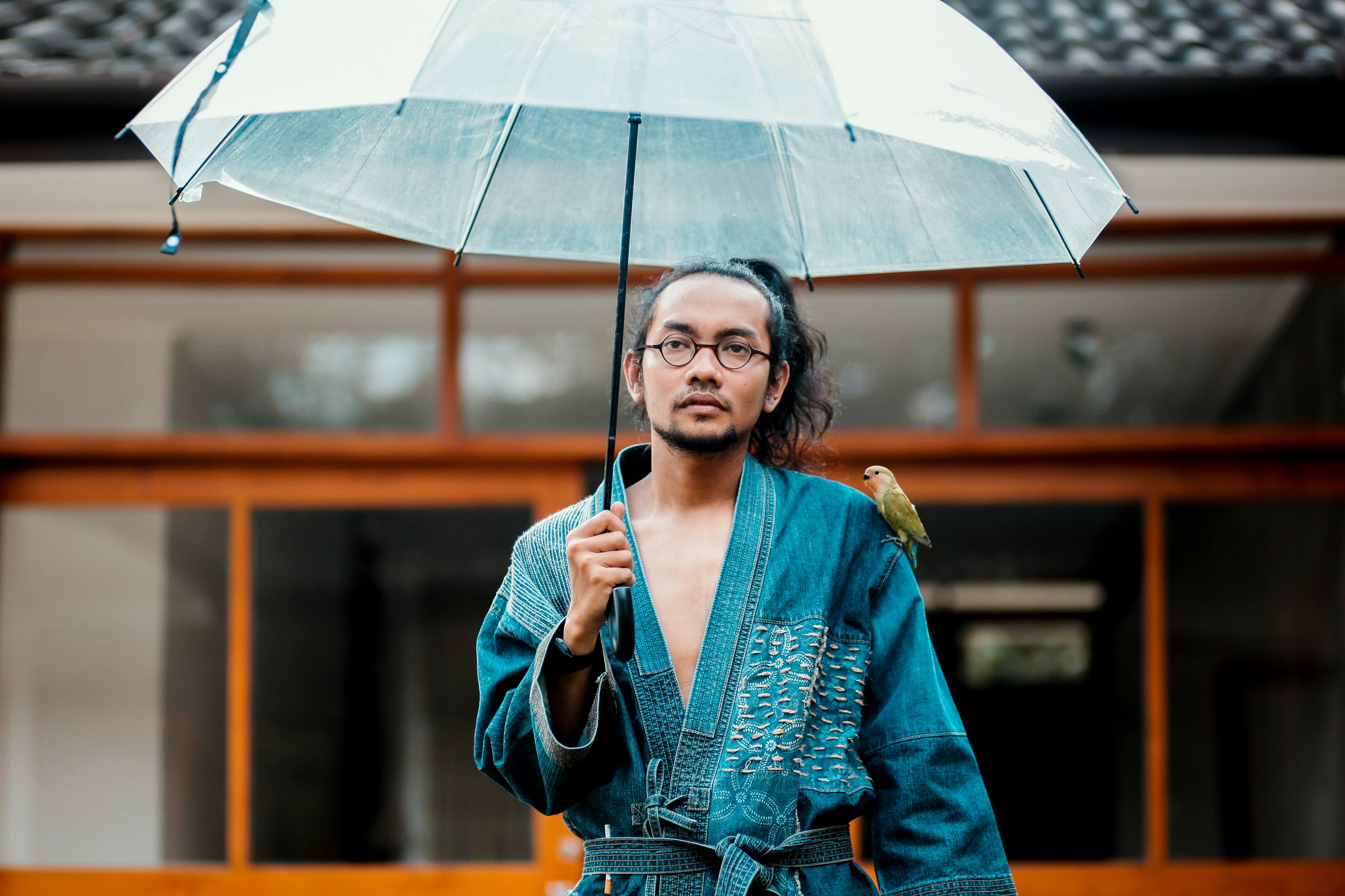 A Japanese man in traditional dress stands under an umbrella in the rain