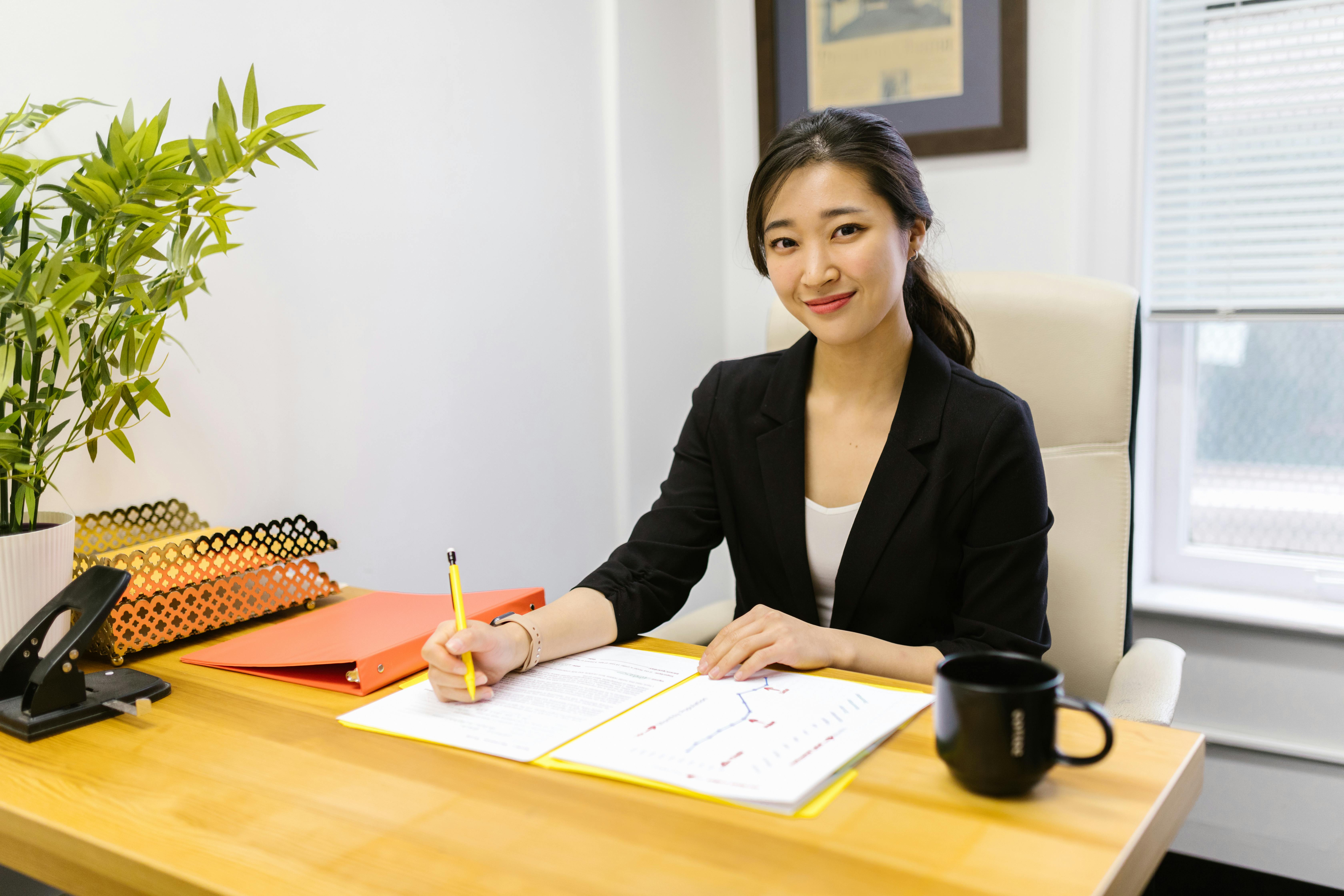 A Japanese business woman sits at her desk, pen in hand