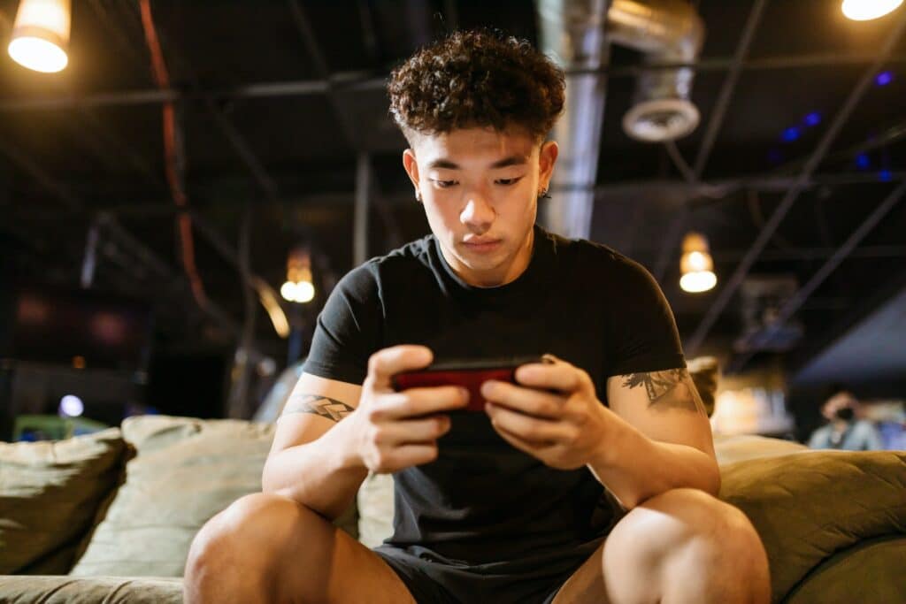 curly-haired-asian-man-playing-mobile-games-while-sitting-on-sofa