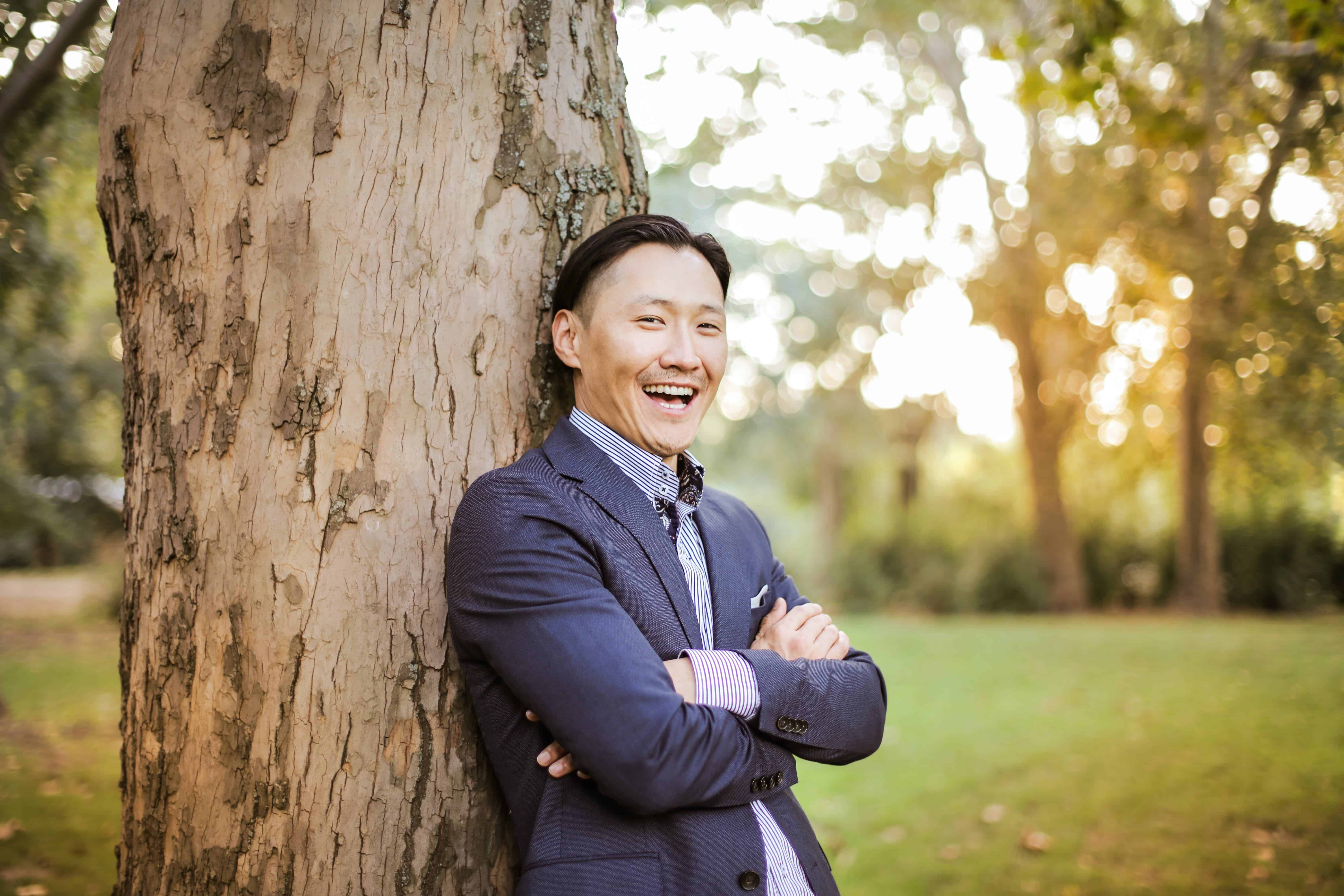 A man wearing a suit standing by a tree and smiling