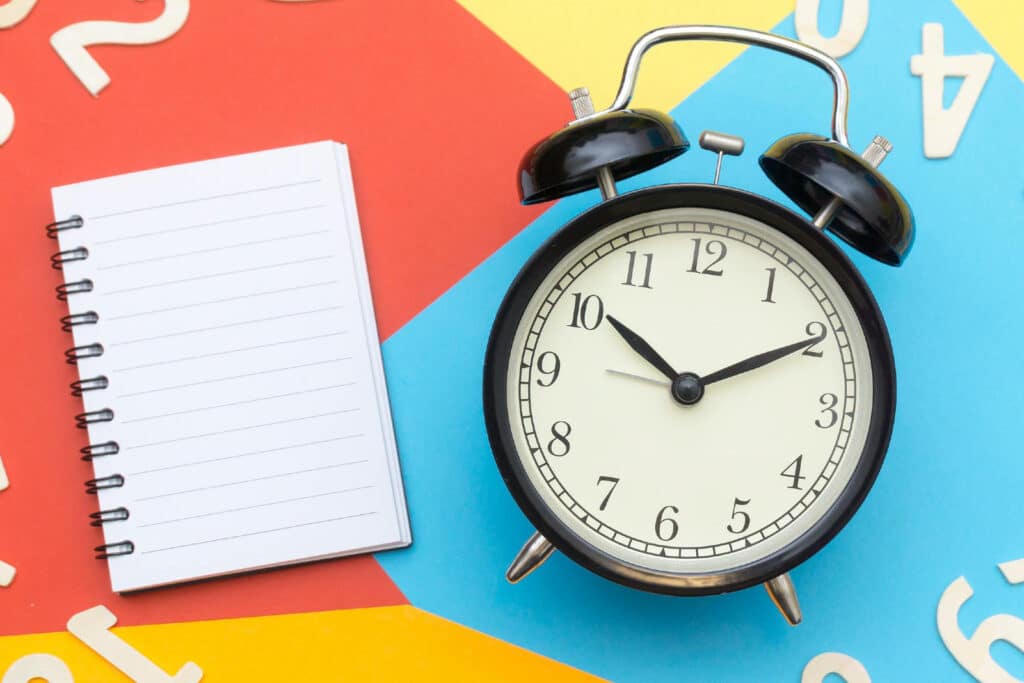 Clock next to notebook on colorful background