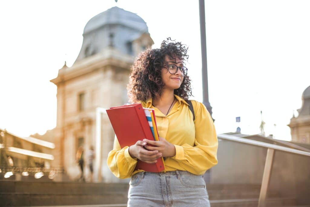 female-student-in-a-yellow-shirt-holding-a-red-binder-and-books