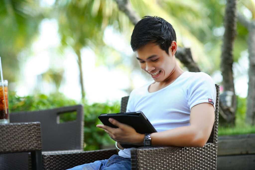 man-smiling-as-he-browses-through-tablet-against-tropical-background