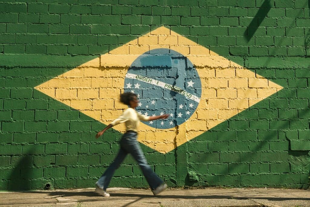 Photo by Bia Santana: https://www.pexels.com/photo/girl-walking-on-street-with-brazilian-flag-on-wall-16162211/