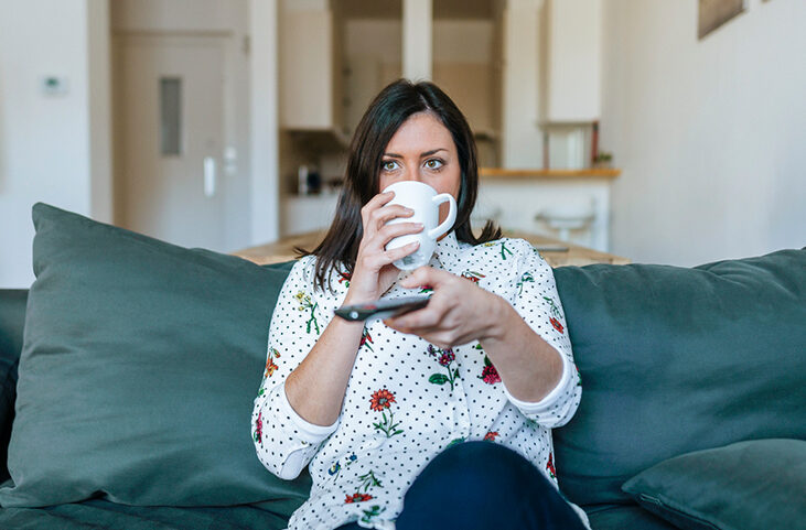 woman sitting on the couch drinking coffee while watching TV