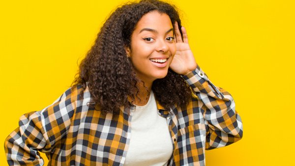 woman putting a hand to her ear in front of a yellow background
