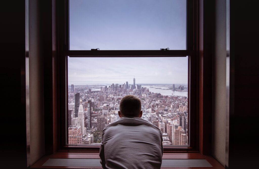 man looking out the apartment window at a big city