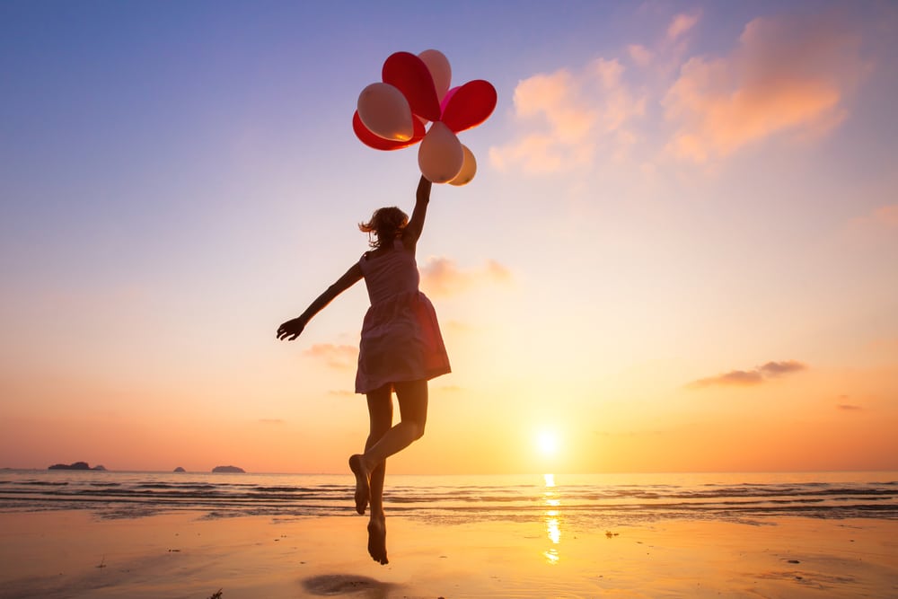 girl jumping with balloons on a beach