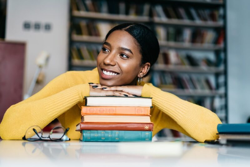 woman-smiling-with-her-head-resting-on-a-pile-of-books