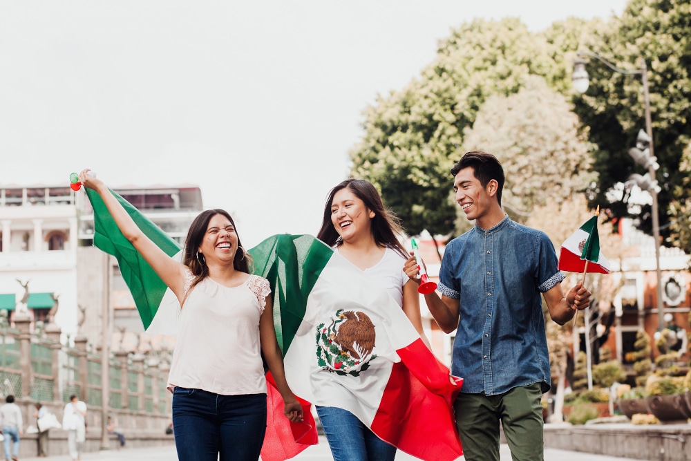 three hispanic adults carrying the mexican flag down the street