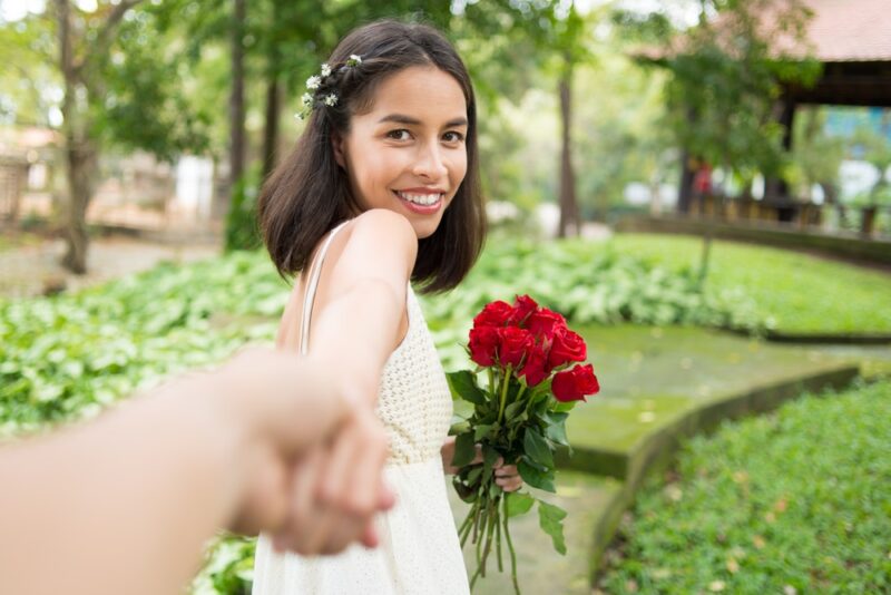 young woman holding someone's hand in a garden with roses