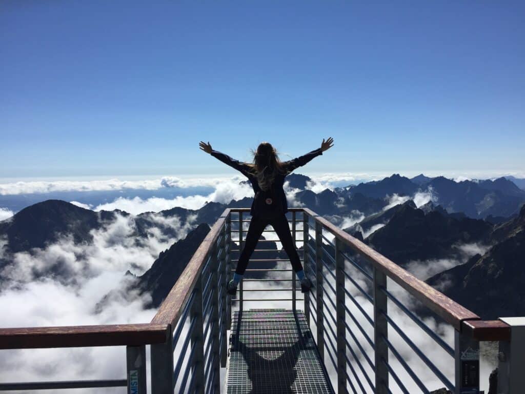 person-standing-on-rails-with-arms-open-facing-the-mountains-covered-by-clouds