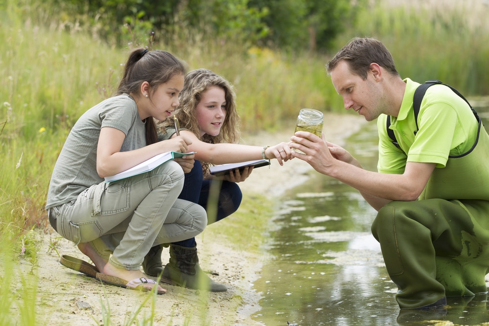 teacher-and-students-observing-water-sample-outdoors