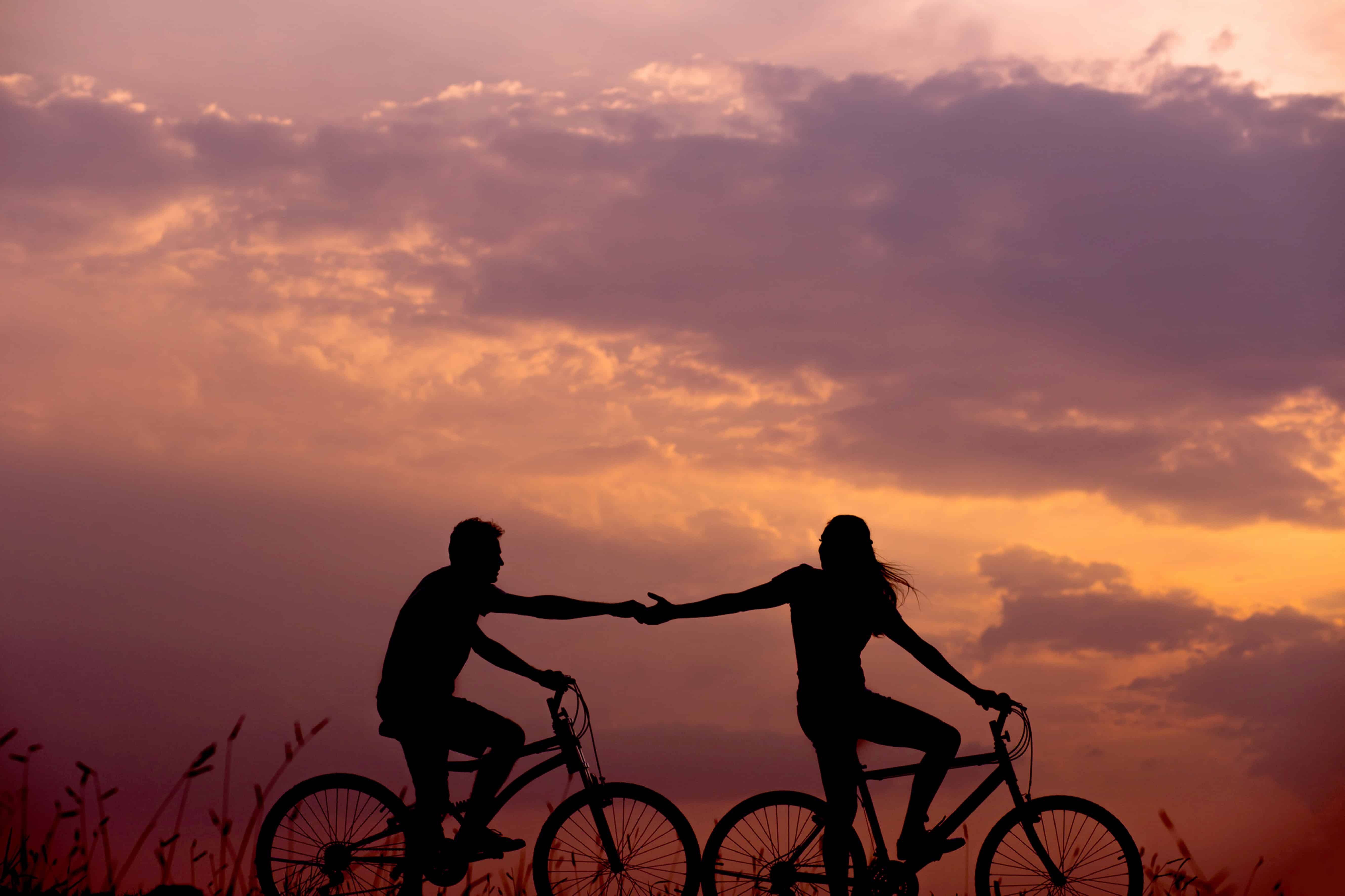 A couple holds hands while cycling