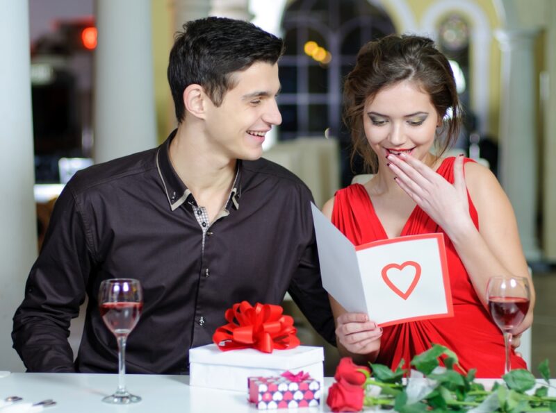 man gives woman gift and card at romantic dinner