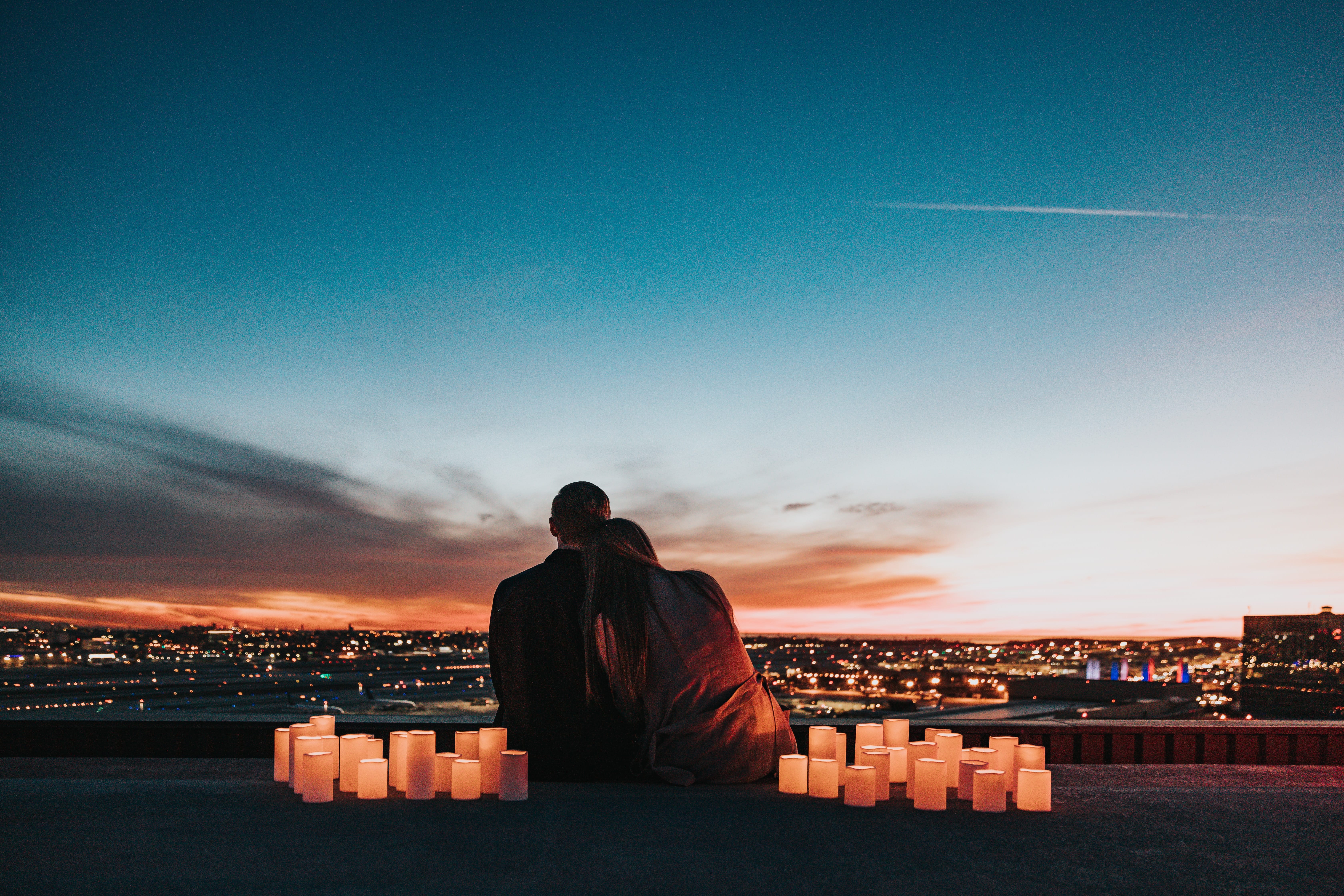 A couple sits on a building top at sunset