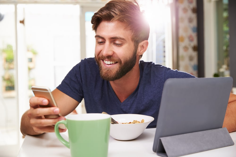 man-smiling-looking-at-phone-over-breakfast
