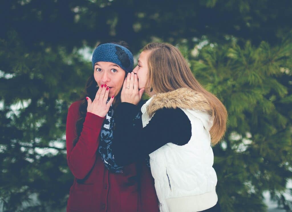 woman-in-black-and-white-winter-wear-whispering-in-another-womans-ear