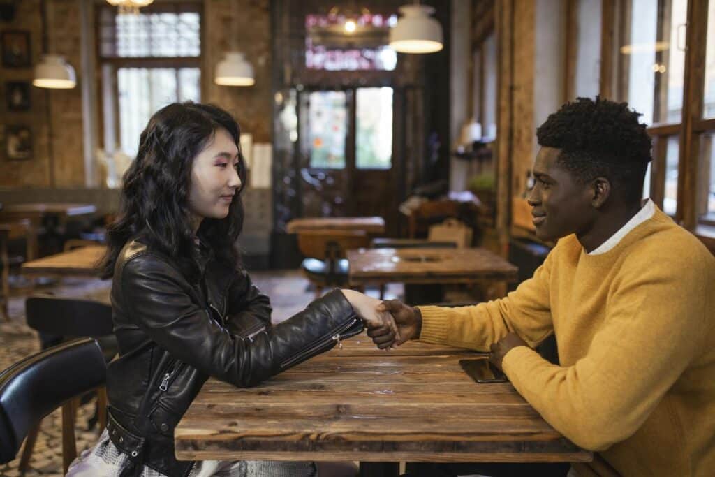 asian-woman-and-black-man-holding-hands-over-wooden-table-in-cozy-restaurant